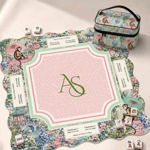 May include: A square mahjong mat with scalloped edges featuring a chinoiserie pattern of monkeys, pagodas, and flowers in pink, green, and blue. The centre has a pink geometric pattern with the green monogram AS. Includes a matching zippered case.