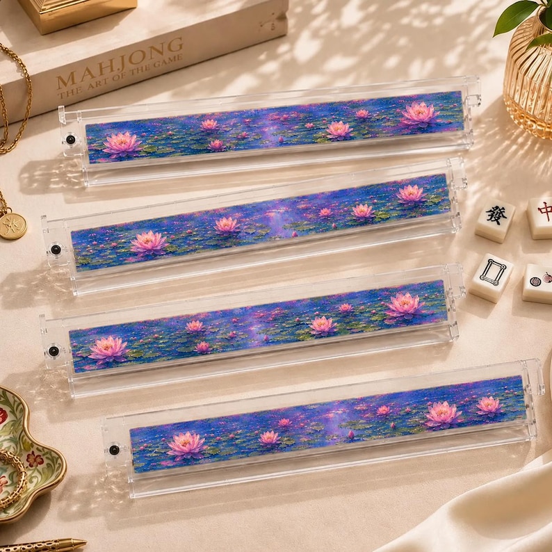 Peut inclure: Quatre supports de tuiles de mah-jong en acrylique transparent avec un motif imprim&eacute; vif de n&eacute;nuphars roses flottant sur un &eacute;tang bleu profond. Chaque support rectangulaire poss&egrave;de une petite vis noire sur le c&ocirc;t&eacute; gauche et un motif floral.