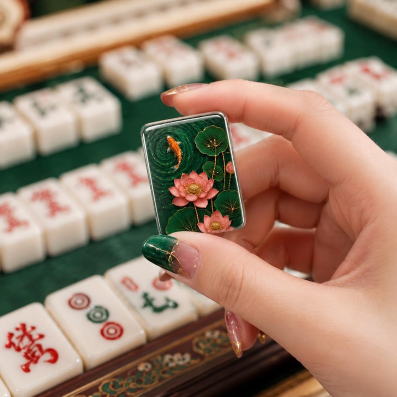 May include: A rectangular mahjong tile featuring a detailed relief design of a vibrant orange koi fish swimming in a deep green pond with pink lotus flowers and dark green lily pads. The tile has a glossy finish and metallic gold accents.
