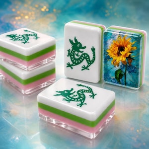 Op de afbeelding: Vier rechthoekige mahjongtegels met een gelaagd ontwerp bestaande uit een witte bovenkant, een groene middenlaag en een roze basis. Drie tegels tonen een groene draakafbeelding, terwijl één tegel een gedetailleerde zonnebloemillustratie bevat.