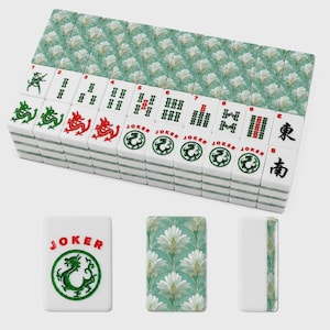 May include: A set of rectangular mahjong tiles featuring a white face with green and red ink designs, including dragon symbols, numbered bamboo patterns, and Joker text. The reverse side displays a repeating white floral pattern on a teal background.