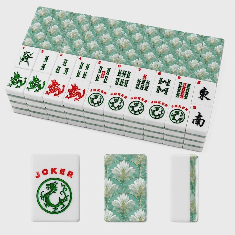 May include: A set of rectangular mahjong tiles featuring a white face with green and red ink designs, including dragon symbols, numbered bamboo patterns, and Joker text. The reverse side displays a repeating white floral pattern on a teal background.