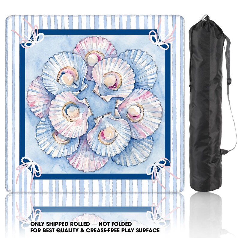 May include: A square play mat featuring a watercolor illustration of pink and white scallop shells with pearls on a light blue background, framed by blue and white stripes and pink bows, accompanied by a black cylindrical carrying bag.