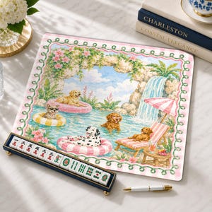 Peut inclure: Un tapis de mah-jong carré présentant une illustration colorée de chiens nageant et se relaxant dans une piscine avec une cascade, encadré par une bordure à carreaux roses et blancs. Un support bleu foncé avec des tuiles blanches est au premier plan.