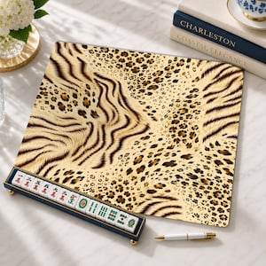 Peut inclure: Un tapis de mah-jong carré avec un motif animalier beige, marron et noir composé de rayures de tigre et de taches de léopard. Un support bleu foncé contient une rangée de tuiles de mah-jong blanches avec des caractères et symboles rouges, verts et noirs.