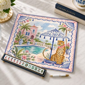 Könnte beinhalten: Ein quadratisches Dekotablett mit einer Aquarellillustration eines Leoparden, der an einem Pool vor einer rosa Villa sitzt, umrahmt von einer blau-weißen Bordüre. Ein passender Mahjong-Fliesenhalter mit zehn Spielsteinen liegt davor.