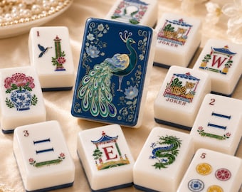 May include: A collection of white mahjong tiles featuring colorful illustrations, including a central tile with a blue background and a peacock, alongside tiles depicting a dragon, flowers in a vase, the letters E and W, and joker labels.