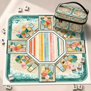 May include: A square mahjong mat featuring a beach scene with colorful umbrellas and lounge chairs, centered by a striped octagon. A matching patterned carrying case sits in the corner, accompanied by several scattered white mahjong tiles.