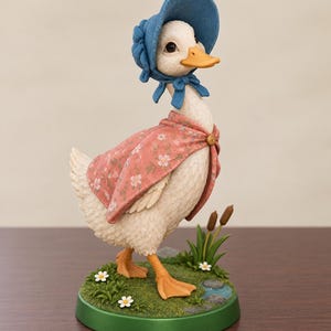 May include: A white duck figurine wearing a blue bonnet and a pink floral cape. The duck stands on a circular green base decorated with grass, small white flowers, and two brown cattails. The duck has an orange beak and orange webbed feet.