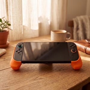 Könnte beinhalten: Eine tragbare Spielkonsole mit schwarzem Bildschirm und schwarzen Controllern, die beidseitig mit einer leuchtend orangefarbenen Schutzhülle versehen ist. Das Gerät verfügt über schwarze Standardtasten, ein Steuerkreuz und einen blau akzentuierten Joystick.