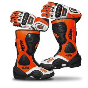 Puede incluir: Un par de botas de moto y guantes a juego en color naranja, blanco y negro. Las botas presentan el logotipo de KTM Racing Team y paneles protectores negros. Los guantes muestran el logotipo de Red Bull y tienen protección reforzada.