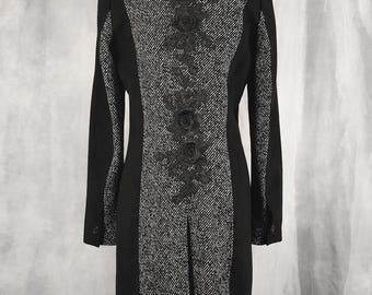 May include: A long-sleeved coat featuring a black and white tweed center panel and side panels, accented by a vertical black floral lace applique down the back. The garment has a high collar, solid black sleeves, and a structured, fitted silhouette.