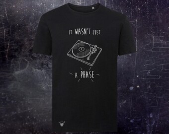 May include: A black short-sleeved t-shirt featuring a white line drawing of a record player in the center. Above the graphic is the text IT WASN'T JUST and below is the text A PHASE. A small white skull icon is located at the bottom left corner.