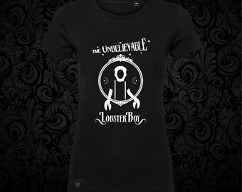 May include: A black short-sleeved t-shirt featuring a white graphic print. The design includes the text "THE UNBELIEVABLE" above and "LOBSTER BOY" below a circular frame containing a silhouette of a figure with lobster claw hands.