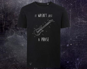 May include: A black short-sleeved t-shirt featuring a white line-art illustration of an electric guitar centered on the chest. Above the guitar is the text "IT WASN'T JUST" and below it is the text "A PHASE" in a simple, clean white font.
