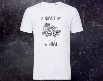 May include: A white short-sleeved t-shirt featuring a black line art graphic of two roller skates in the center. Above the skates, the text reads IT WASN'T JUST, and below the skates, the text reads A PHASE, with small decorative lines.