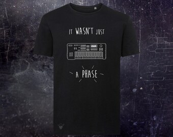 May include: A black short-sleeved t-shirt featuring a white line drawing of a synthesizer keyboard in the center. Above the keyboard is the text "IT WASN'T JUST" and below it is the text "A PHASE" with small radiating lines around the word phase.