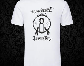 May include: A white short-sleeved t-shirt featuring a black graphic print. The design includes the text "THE UNBELIEVABLE" above a circular frame containing a silhouette of a figure with lobster claws, with the text "LOBSTER BOY" printed below.