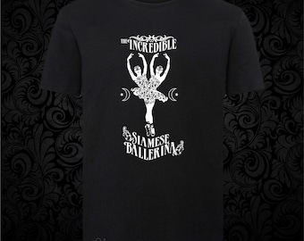 May include: A black short-sleeved t-shirt featuring a white graphic print of a conjoined ballerina figure. The text reads THE INCREDIBLE SIAMESE BALLERINA, accompanied by crescent moon and star symbols, with a small skull icon near the bottom hem.