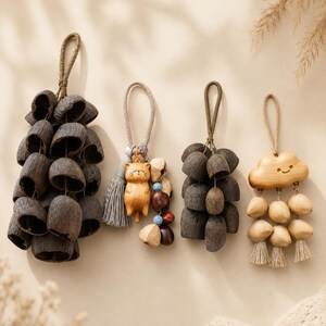 May include: Four hanging ornaments featuring natural materials. Two are clusters of dark brown, hollowed seed pods on rope loops. One features a carved wooden cat figure with a blue and tan tassel. One features a carved wooden cloud with dangling light-colored seeds.