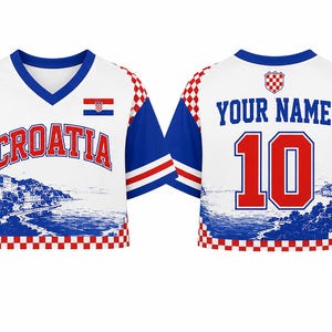 May include: A white V-neck jersey with blue sleeves and a red and white checkered pattern. The front features the text CROATIA, a small Croatian flag, and a blue coastal landscape graphic. The back displays the text YOUR NAME and the number 10.