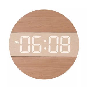 May include: A circular digital clock with a light brown wood grain finish. A horizontal band across the centre features a light beige panel displaying the white digital time 06:08 and the letters PM on the left side in a clear sans-serif font.