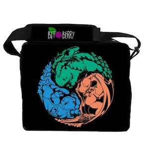 Op de afbeelding: Een zwarte schoudertas met een cirkelvormige afbeelding van drie wezens in groen, blauw en oranje, gerangschikt in een yin-yang patroon. De schouderband toont de tekst BIT BERRY met een klein frambozenicoontje boven de letter I.