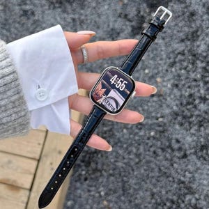Op de afbeelding: Een smartwatch met een rechthoekige zilveren behuizing en een zwarte lederen horlogeband met krokodillenprint. Het digitale display toont de tijd 4:55 en de tekst CENTUR. Het horloge heeft een zilveren gesp en een gepolijste afwerking.