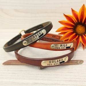 May include: Three leather collars in black, tan, and brown, each featuring a brass identification plate. The plates are engraved with the names DEBBER, MILO, and ROLAND, along with phone numbers. Each plate is secured with two brass rivets.