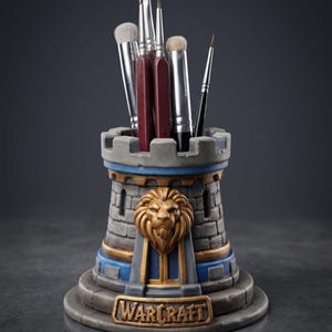 Peut inclure: Un organisateur de bureau en forme de château gris et bleu avec un emblème de tête de lion doré et le texte WARCRAFT sur la base. La structure a un bord supérieur crénelé et contient cinq pinceaux variés aux manches bordeaux et noirs.