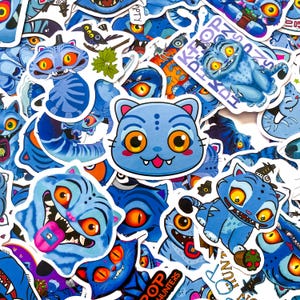 May include: A collection of die-cut stickers featuring blue cat-like creatures with large orange eyes, sharp teeth, and striped patterns. Some stickers show the text K-POP HUNTERS and POP HUNTERS, while others depict the creatures with tongues out.
