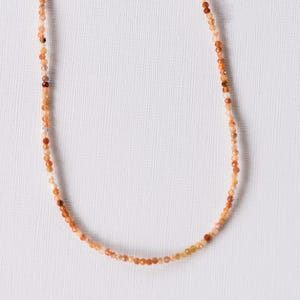 Peut inclure: Un collier délicat composé de petites perles rondes orange et blanches.
