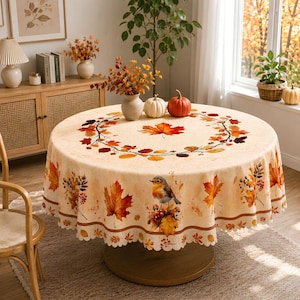 Puede incluir: Un mantel redondo con una base de color crema y un estampado de temática otoñal. El diseño incluye una corona central de coloridas hojas de arce, follaje naranja y rojo disperso y una ilustración detallada de un pequeño petirrojo.
