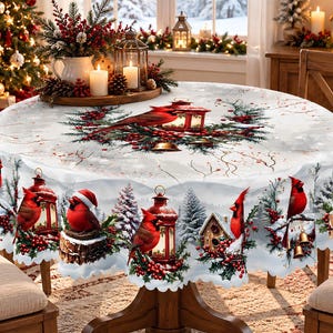 May include: A round tablecloth featuring a winter scene with red cardinals, snow-covered pine trees, red berries, and lanterns. The design includes a central motif of a cardinal and lantern surrounded by greenery on a white background.