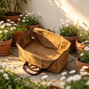 May include: A rectangular, open-top tan canvas utility bag with dark brown trim and two sturdy handles. The bag features a structured base and reinforced stitching, with a small white label visible on the interior side panel of the fabric.
