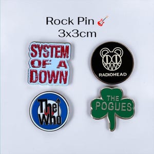 Könnte beinhalten: Vier Metall-Emaille-Anstecknadeln mit einer Größe von jeweils 3x3cm. Eine Nadel zeigt das rot-weiße System of a Down Logo, eine das schwarze Radiohead-Bärenlogo, eine das blau-weiße The Who Zielscheiben-Logo und eine ein grünes Kleeblatt mit dem Text The Pogues.