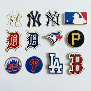 Könnte beinhalten: Eine Sammlung von zwölf Metall-Emaille-Anstecknadeln mit verschiedenen Logos der Major League Baseball-Teams, darunter die New York Yankees, Detroit Tigers, Toronto Blue Jays, Pittsburgh Pirates, New York Mets, Philadelphia Phillies, Los Angeles Dodgers und Boston Red Sox.