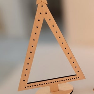 Puede incluir: Un soporte para pendientes de madera con forma de &aacute;rbol de Navidad con una estrella en la parte superior. El &aacute;rbol tiene un soporte y est&aacute; decorado con peque&ntilde;os puntos negros.