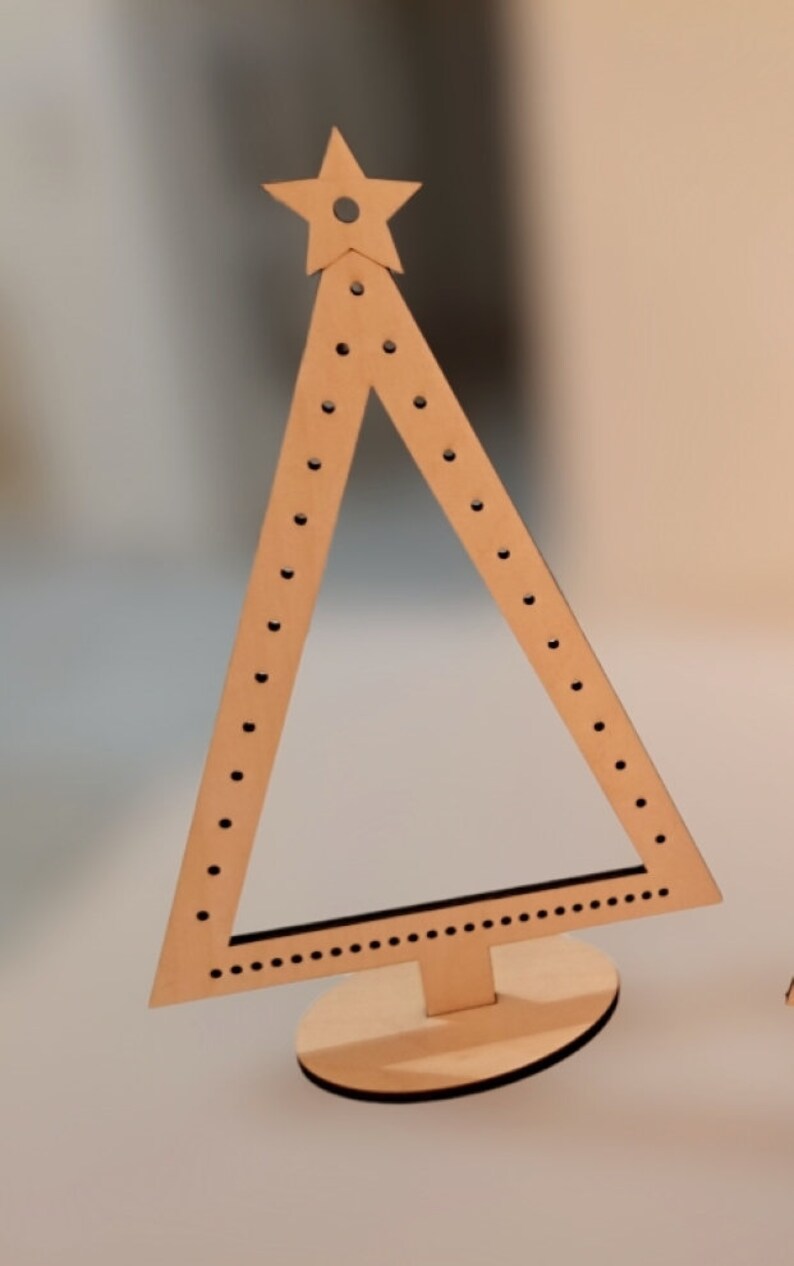 Puede incluir: Un soporte para pendientes de madera con forma de &aacute;rbol de Navidad con una estrella en la parte superior. El &aacute;rbol tiene un soporte y est&aacute; decorado con peque&ntilde;os puntos negros.