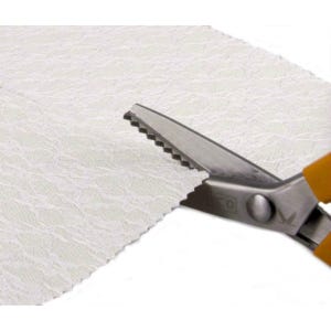 May include: A pair of silver fabric shears with an orange handle cutting a piece of white lace fabric.