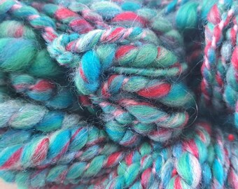 May include: Close-up of a skein of yarn with a mix of blue, green, and red colors. The yarn is soft and fluffy, and it is perfect for knitting or crocheting.