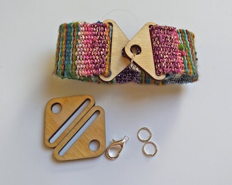 Può includere: Un braccialetto in tessuto intrecciato con un motivo rosa, verde e blu. Il braccialetto ha due chiusure in legno, una a forma di triangolo e l'altra a forma di quadrato con un design ritagliato. Il braccialetto include anche due anelli di giunzione argentati e una chiusura a moschettone argentata.