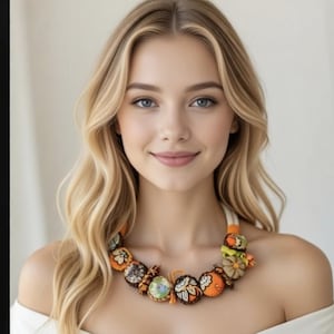 Può includere: Una collana colorata fatta a mano con vari elementi rotondi in tessuto nei toni dell'arancione, marrone e verde. La collana, con un cordoncino bianco, si indossa intorno al collo. Questo gioiello unico presenta una varietà di trame e colori.