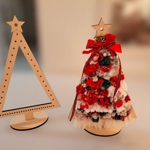 Puede incluir: Dos adornos de &aacute;rbol de Navidad de madera. Uno es un &aacute;rbol simple, plano, triangular con una estrella en la parte superior. El otro es un &aacute;rbol 3D decorado con hilo rojo, blanco y verde y un lazo rojo con el n&uacute;mero 2021 en la parte superior.