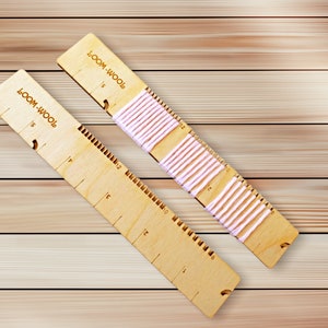 May include: Two wooden loom boards with pink yarn strung across them. The boards are marked with numbers 1 to 12. The text "TOOM-WOOT" is printed on each board.