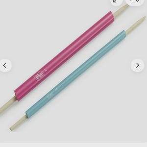 May include: Two knitting needle tools, one pink and one teal, are displayed diagonally. The pink tool is labeled "L" and the teal tool is labeled "M". Both tools have a wooden tip.