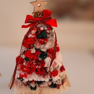 Puede incluir: Un peque&ntilde;o &aacute;rbol de Navidad de madera decorado con hilo rojo, blanco y verde, un lazo rojo y una estrella de madera con el n&uacute;mero 2021.