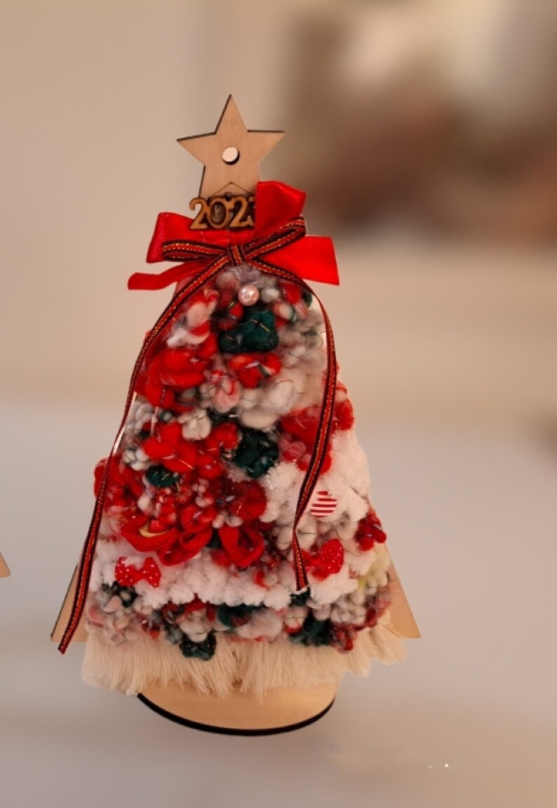 Puede incluir: Un peque&ntilde;o &aacute;rbol de Navidad de madera decorado con hilo rojo, blanco y verde, un lazo rojo y una estrella de madera con el n&uacute;mero 2021.