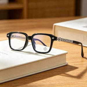 Puede incluir: Gafas rectangulares negras con lentes transparentes que presentan un pequeño emblema de cruz en la lente derecha. Las patillas están adornadas con intrincados detalles metálicos plateados y un motivo de cruz decorativo en la bisagra.