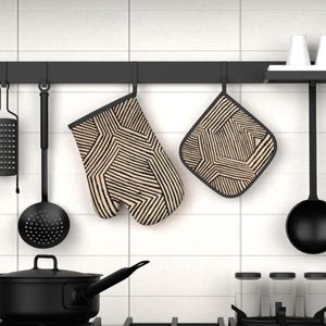 May include: An oven mitt and a square pot holder featuring a beige and black geometric line pattern. These kitchen textiles hang from a black wall-mounted rack alongside various black kitchen utensils, including a skimmer and a ladle.